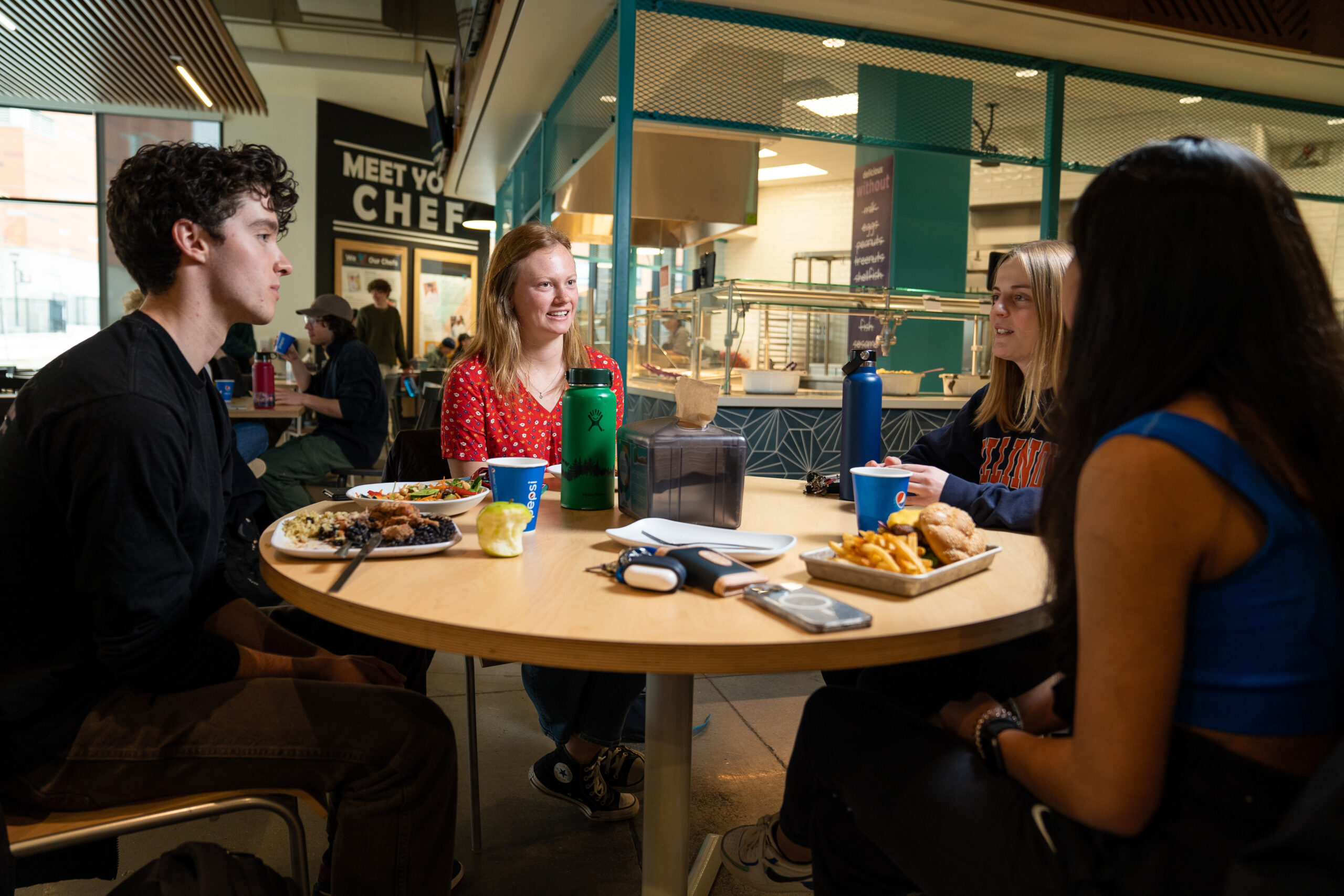 3 Students sitting around a dining table in Kahlert Village talking and eating.